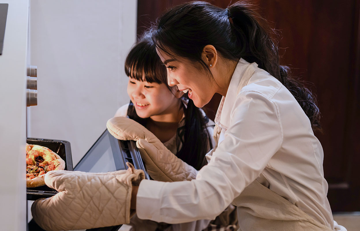 A mother and her daughter take a pizza out of the oven